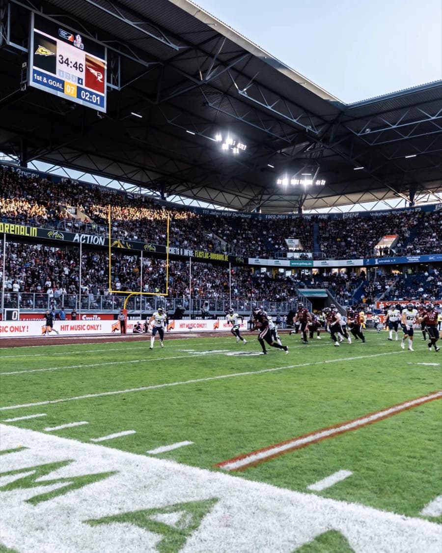 Ein gefülltes Stadion unter Flutlicht während eines Footballspiels.