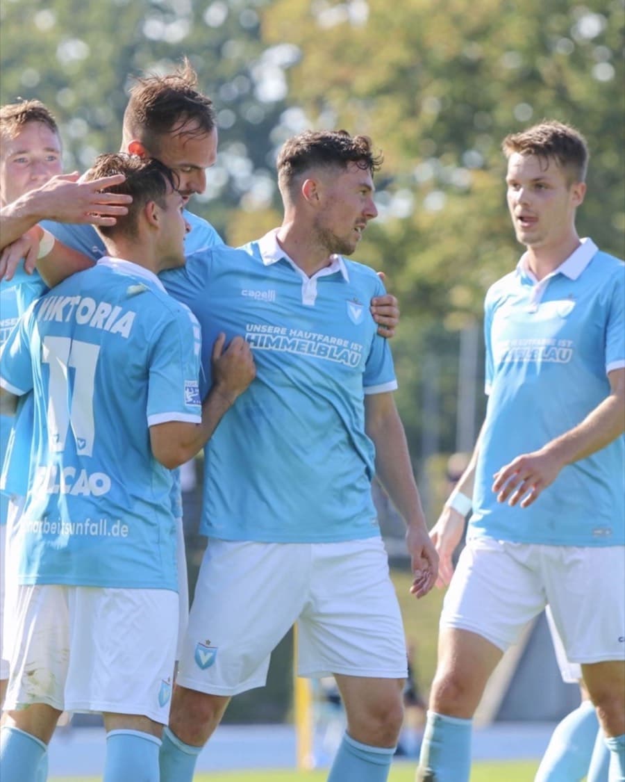Junge Fußballspieler in hellblauen Trikots feiern gemeinsam auf dem Platz.